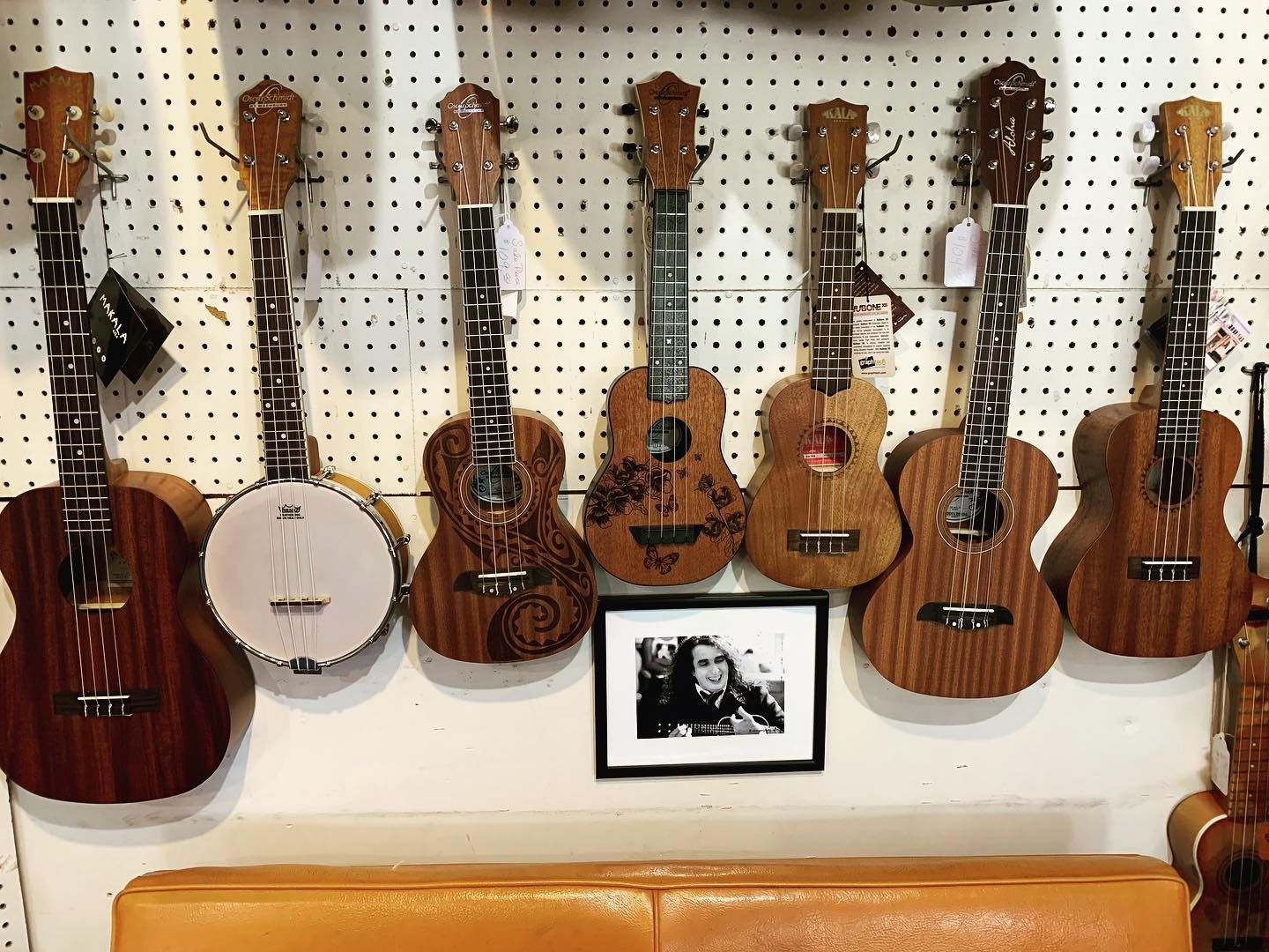 Assorted acoustic guitars and a banjo displayed on a pegboard wall with a framed photo below.