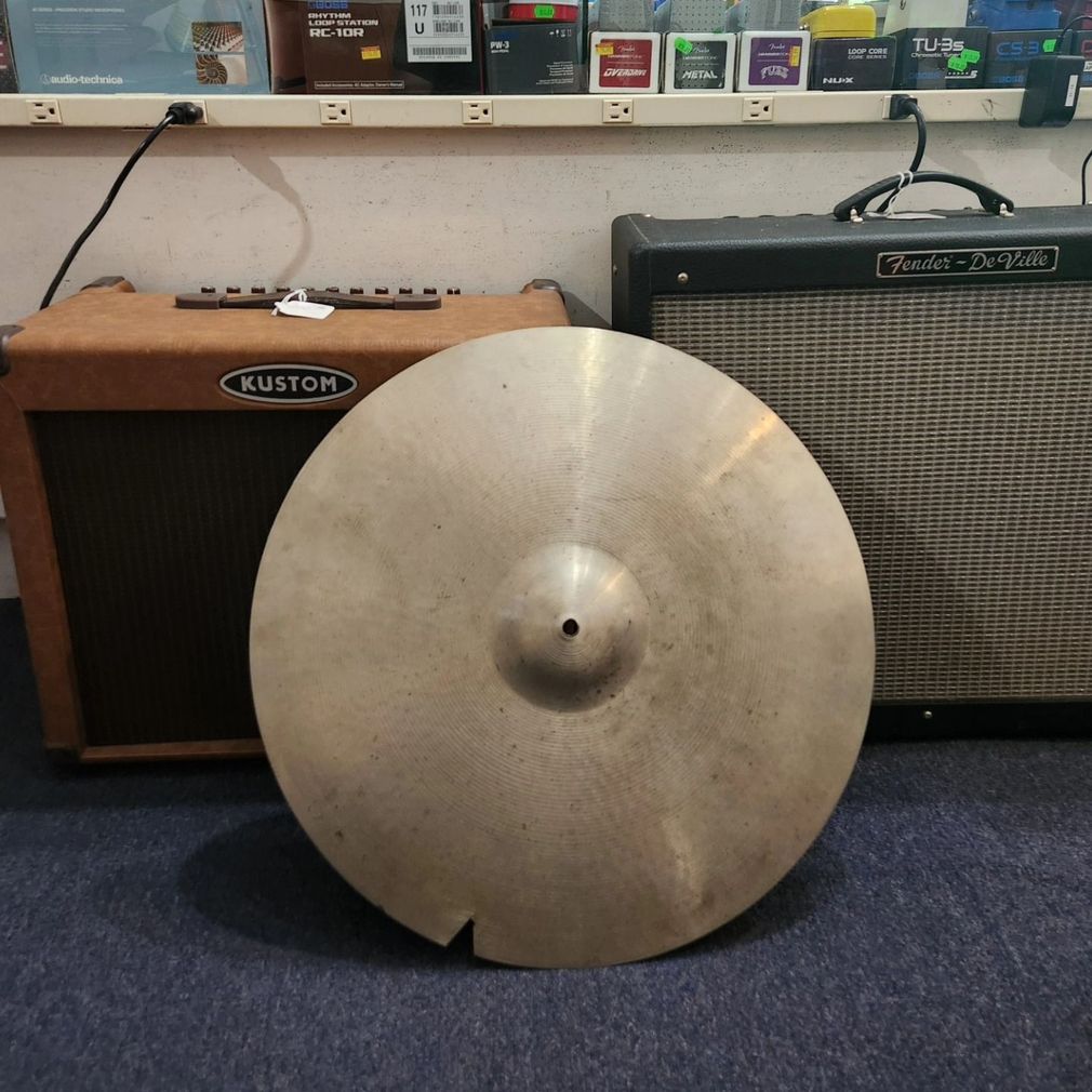 Large silver cymbal leaning in front of two guitar amplifiers in a music store.