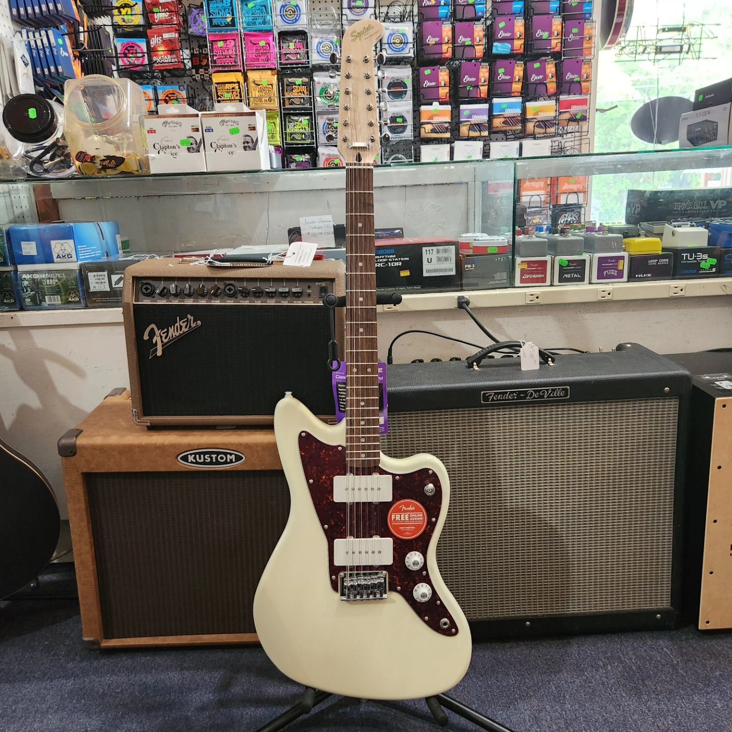 Cream electric guitar on a stand in a music store, with amplifiers behind it.