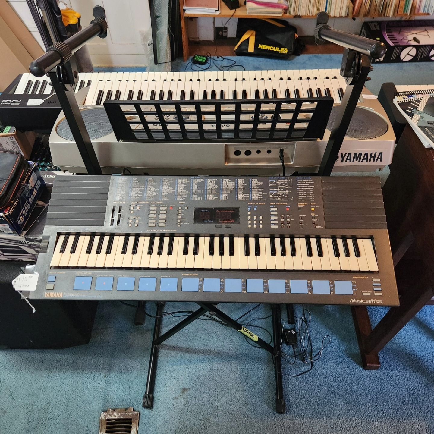 Three Yamaha keyboards on stands in a music room, with microphones and cables nearby.