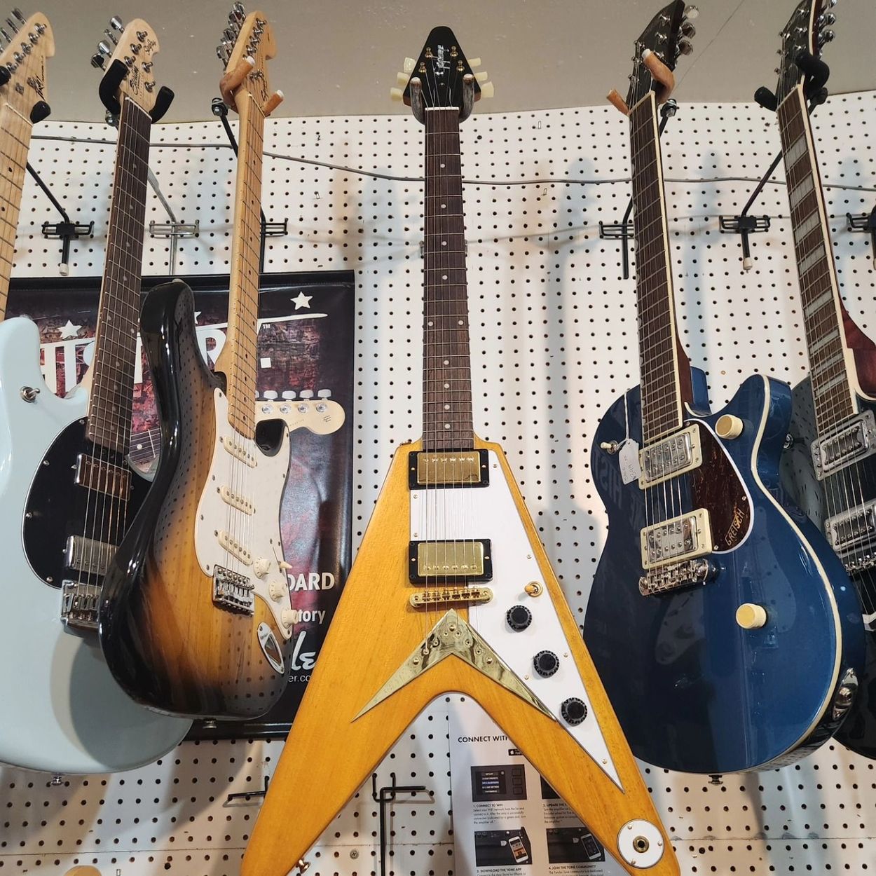 Electric guitars on a pegboard wall, including a yellow V-shaped guitar at center.