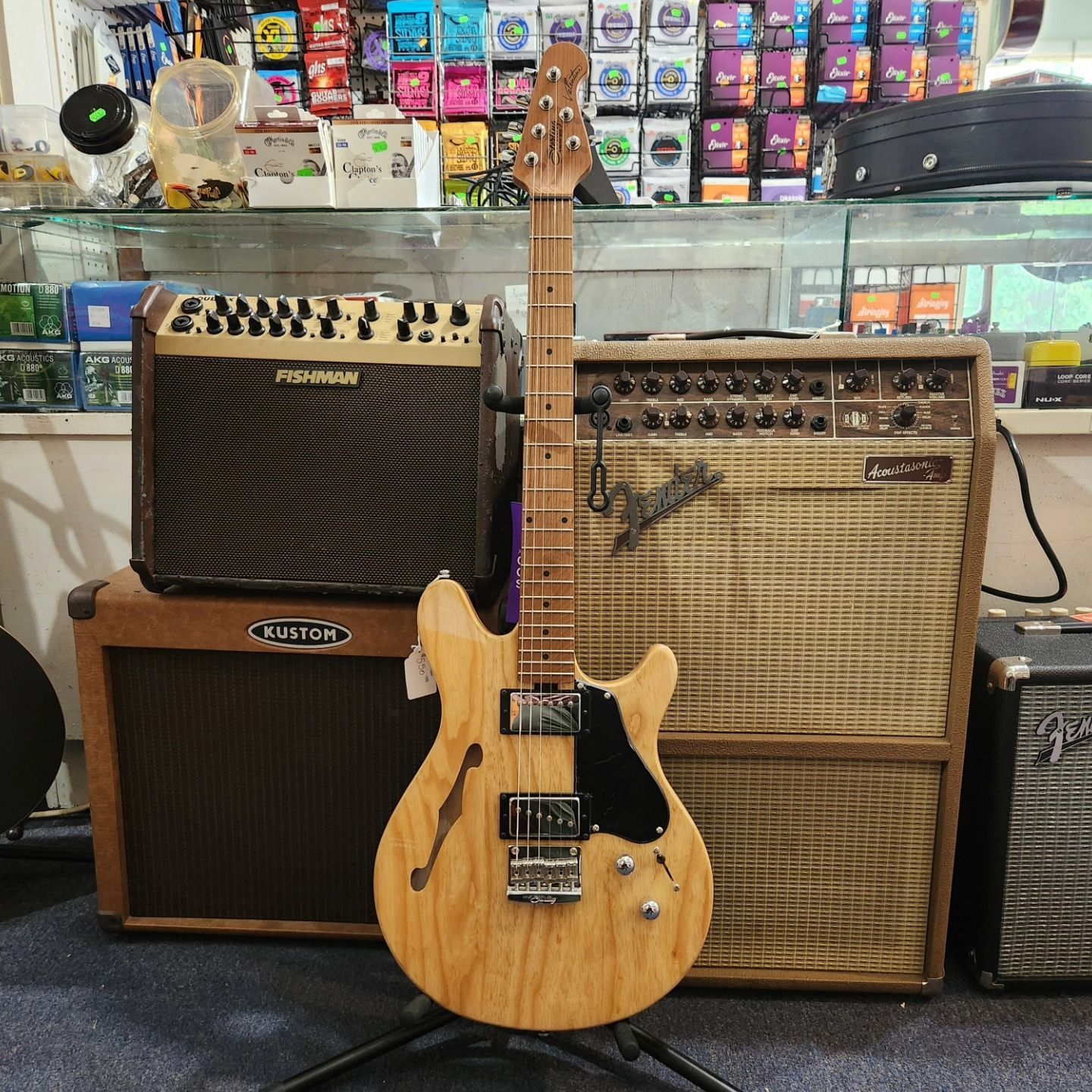 Two electric guitars and amplifiers in a music store display, with a natural wood guitar centered.