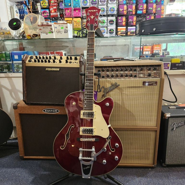 Red electric guitar in front of stacked amplifiers in a music shop.