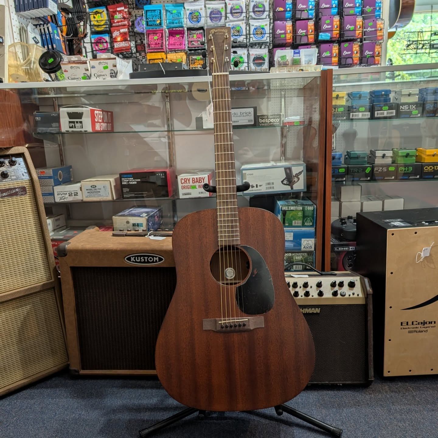 Brown acoustic guitar on display in a music shop, with amps and accessories behind it
