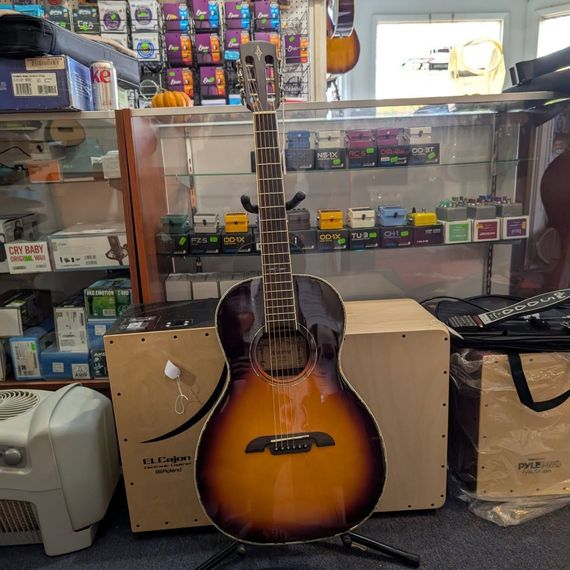 Sunburst acoustic guitar standing in a shop display case, surrounded by music accessories.