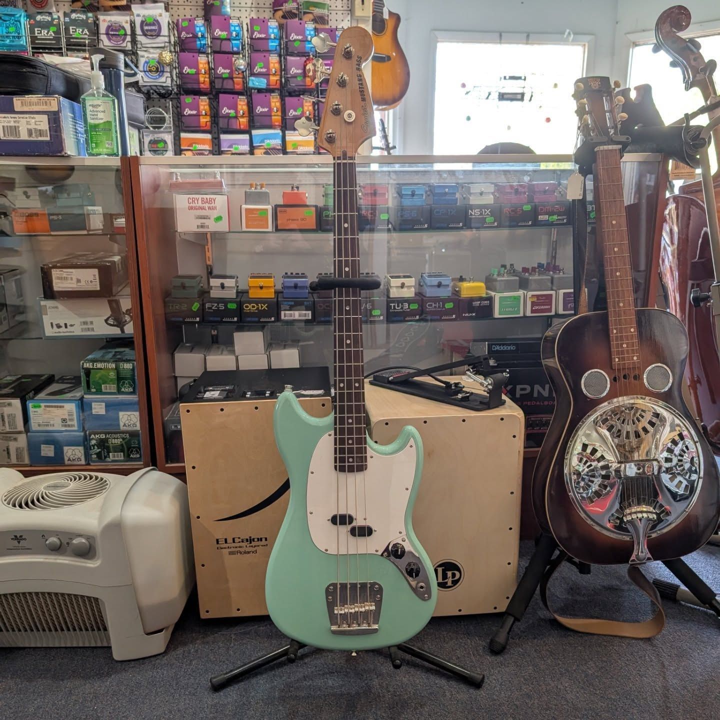 Two guitars on stands in a music shop, with cases and gear displayed behind them.
