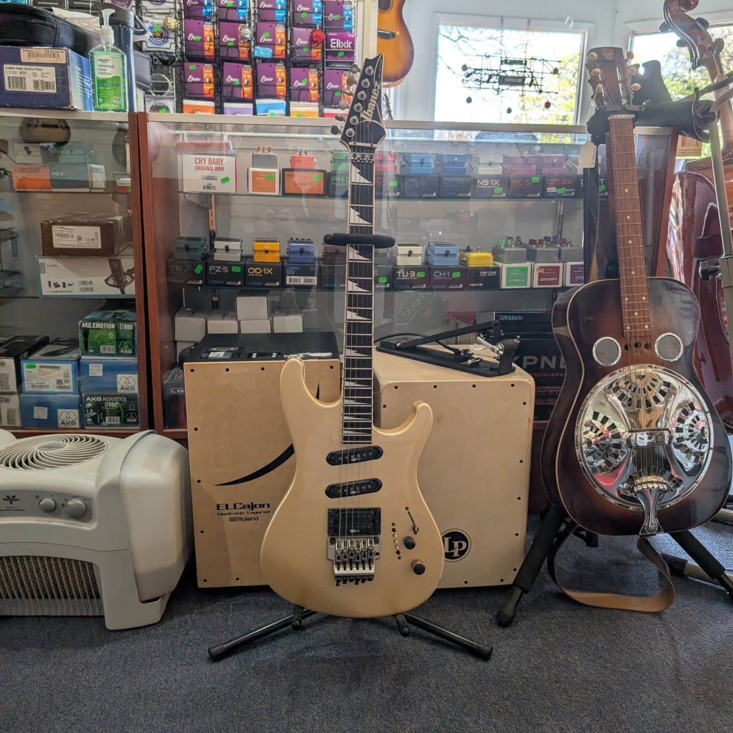 Electric guitar on stand in a music shop, with speaker cabinet and resonator guitar in the background