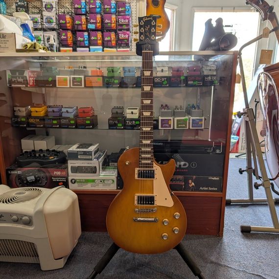 Sunburst electric guitar on a stand in a music shop, with shelves of gear and a black cat figurine behind it
