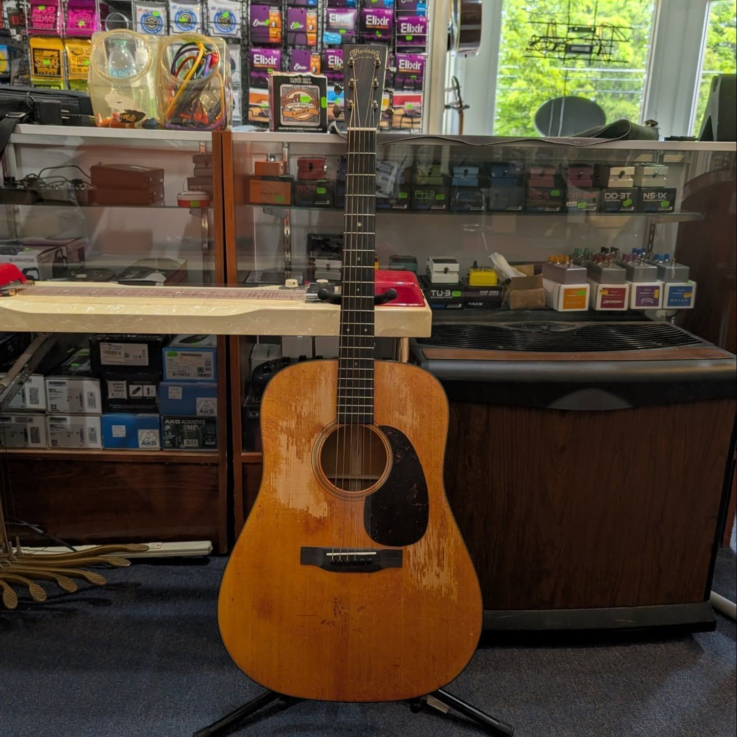 Acoustic guitar on a stand in a music shop, with shelves of guitar accessories behind it.