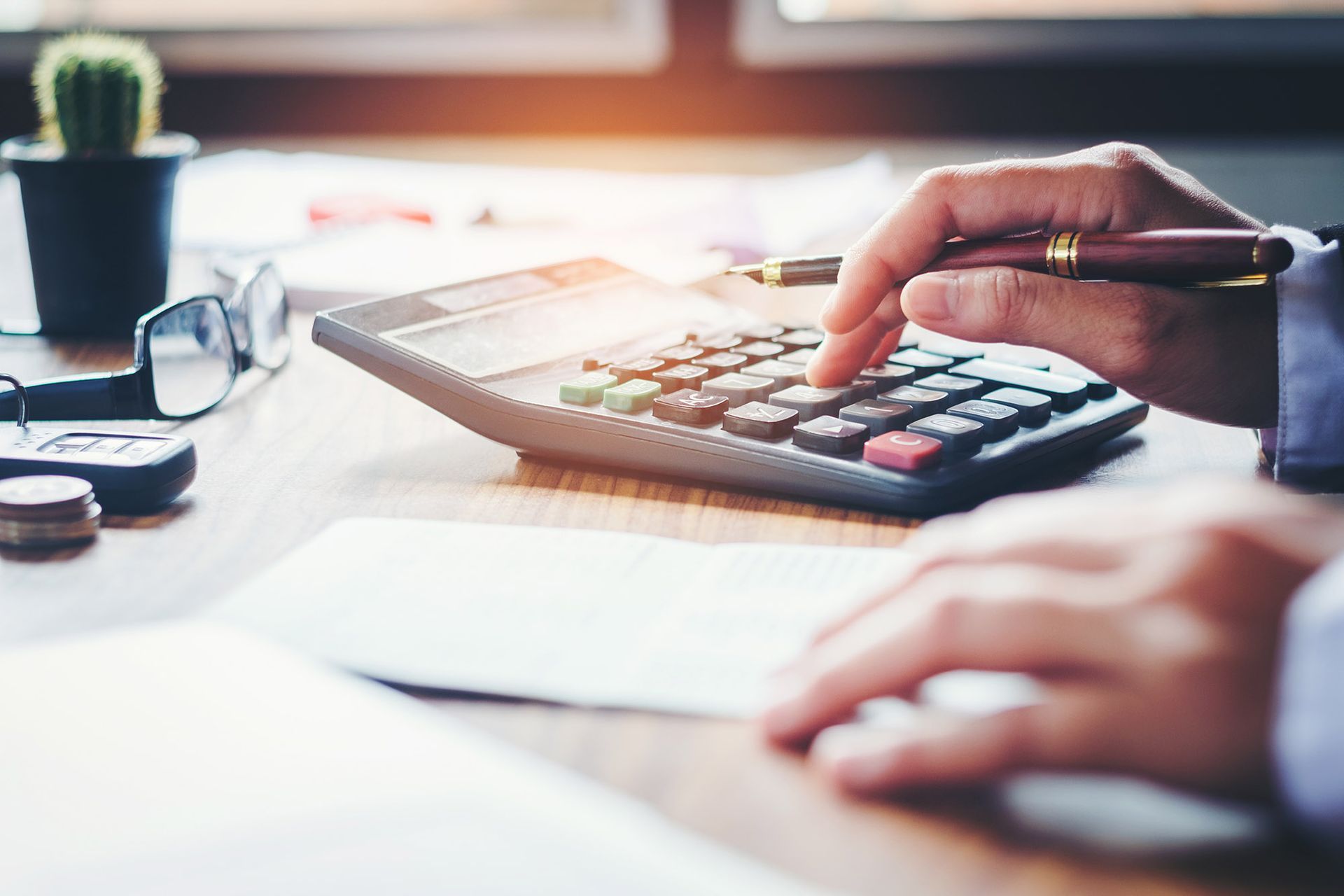 Hands using calculator, document, pen on desk, accounting.