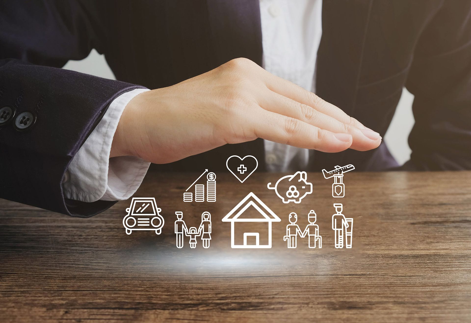 Hand protecting icons of home, family, car, finances, and security, on a wooden table.