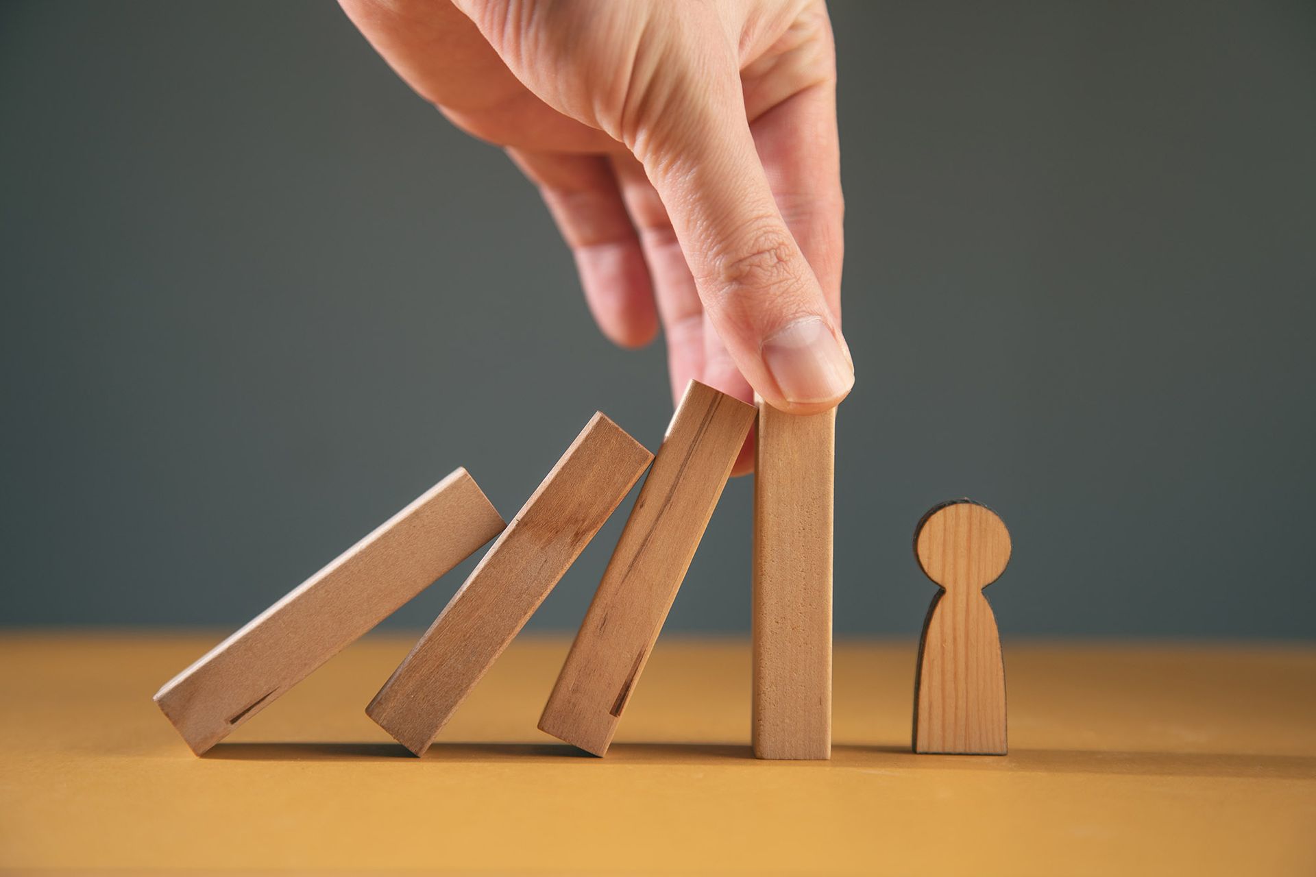 Hand stopping dominoes from falling towards a wooden person-shaped figure.