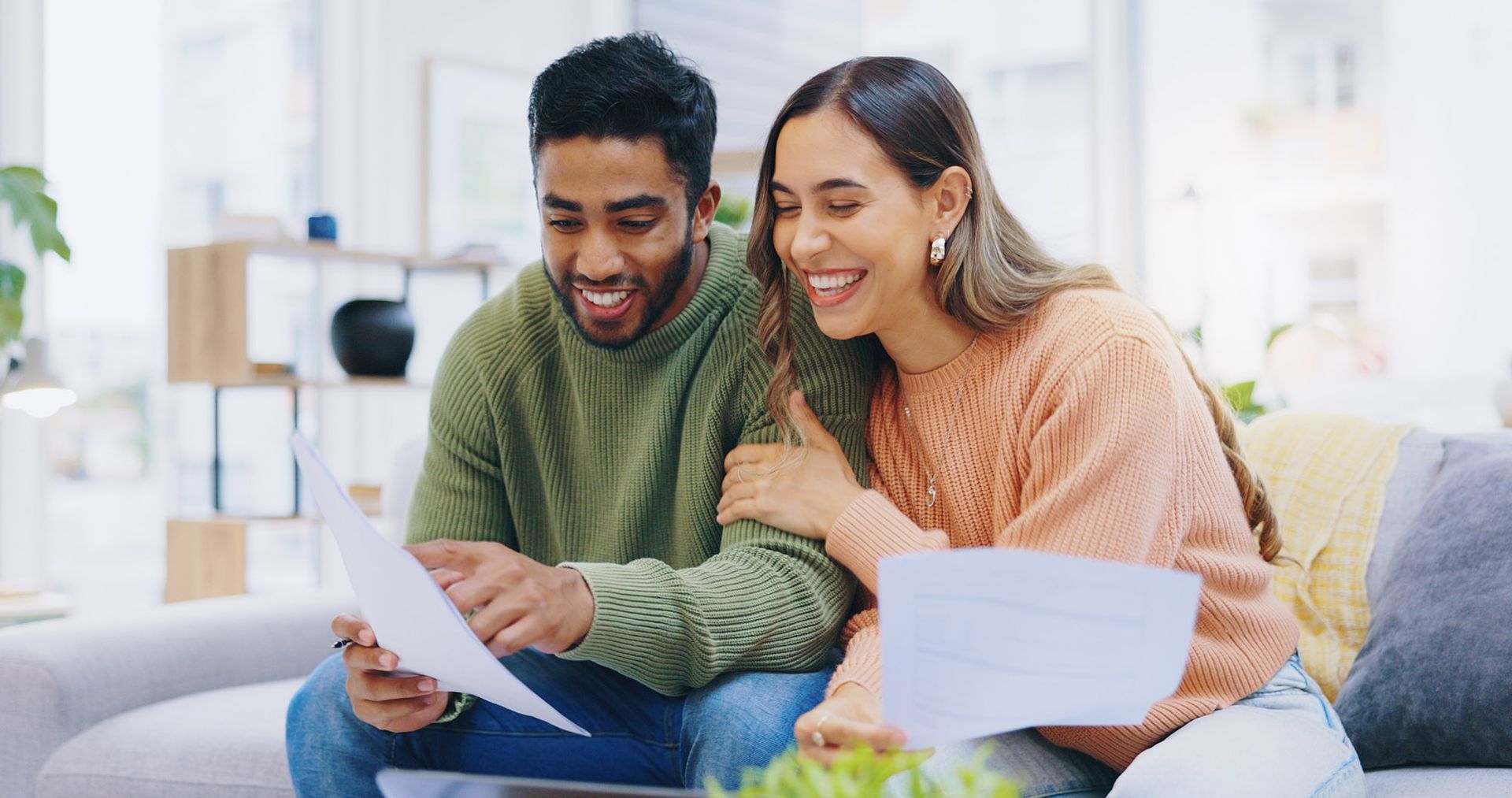 Couple smiling while looking at documents on a couch indoors.