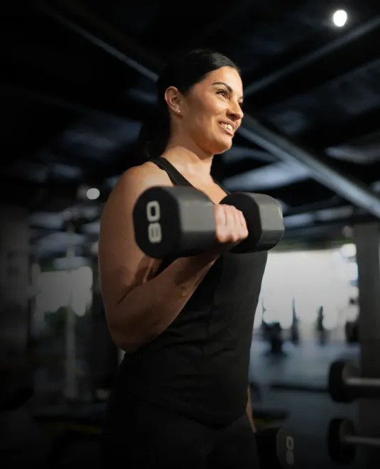Woman lifting dumbbells in a gym, smiling during a workout