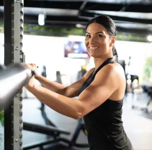 Woman in a gym smiling while holding a metal exercise bar.