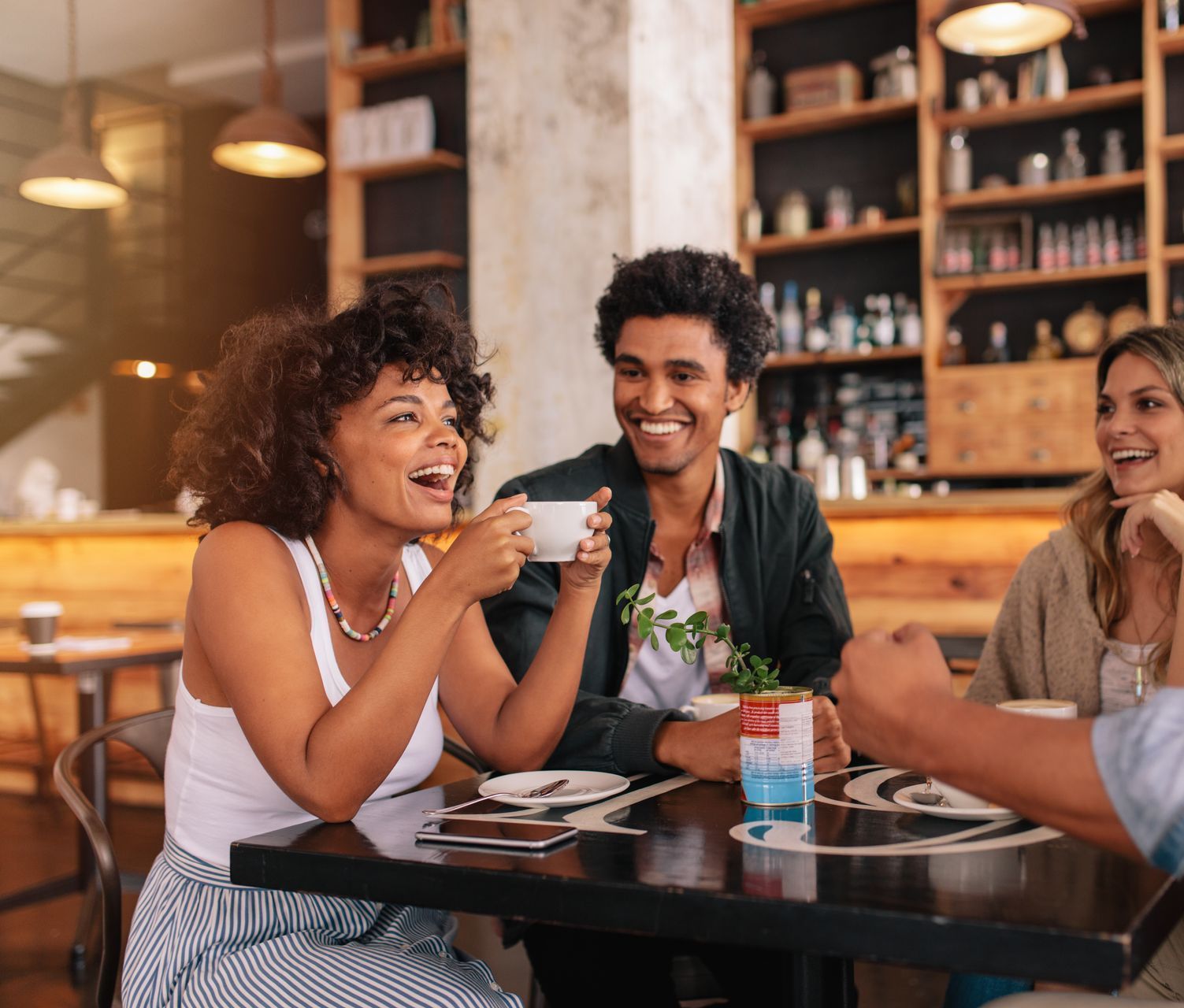 Friends laughing at a table in a cafe, holding coffee cups.