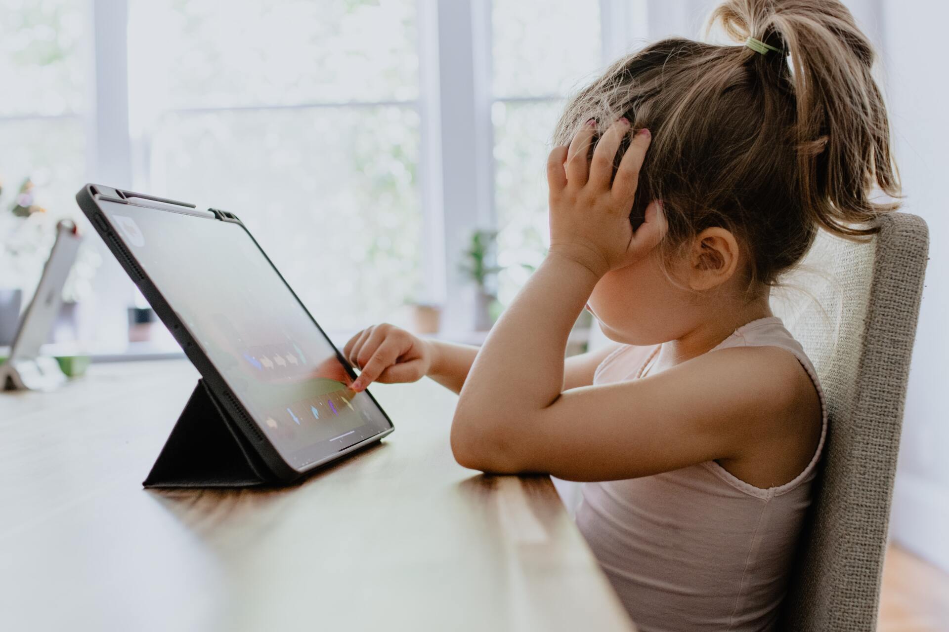 Young girl learning on tablet, head in hand