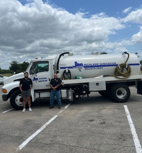 White Richland Sanitation vacuum truck with two people standing beside it in a parking lot under a cloudy sky