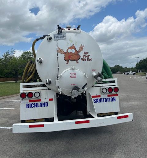 Rear view of a white Richland Sanitation truck with a cartoon logo in a parking lot