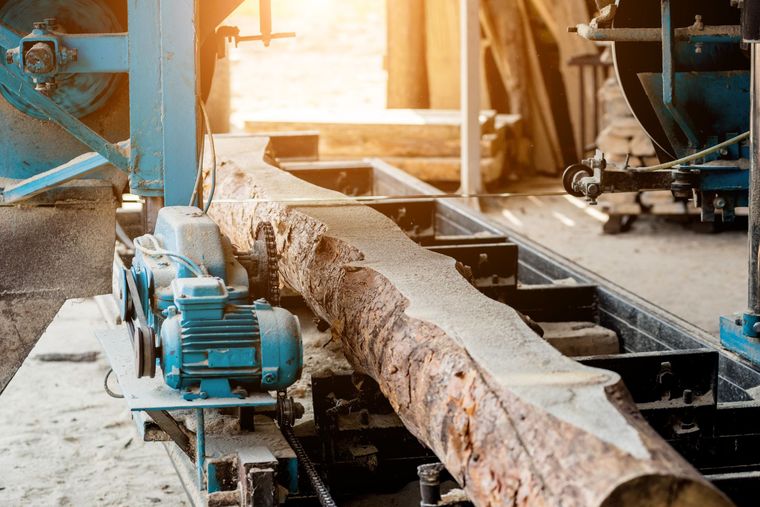 Une grosse bûche est sciée sur une scierie industrielle bleue.
