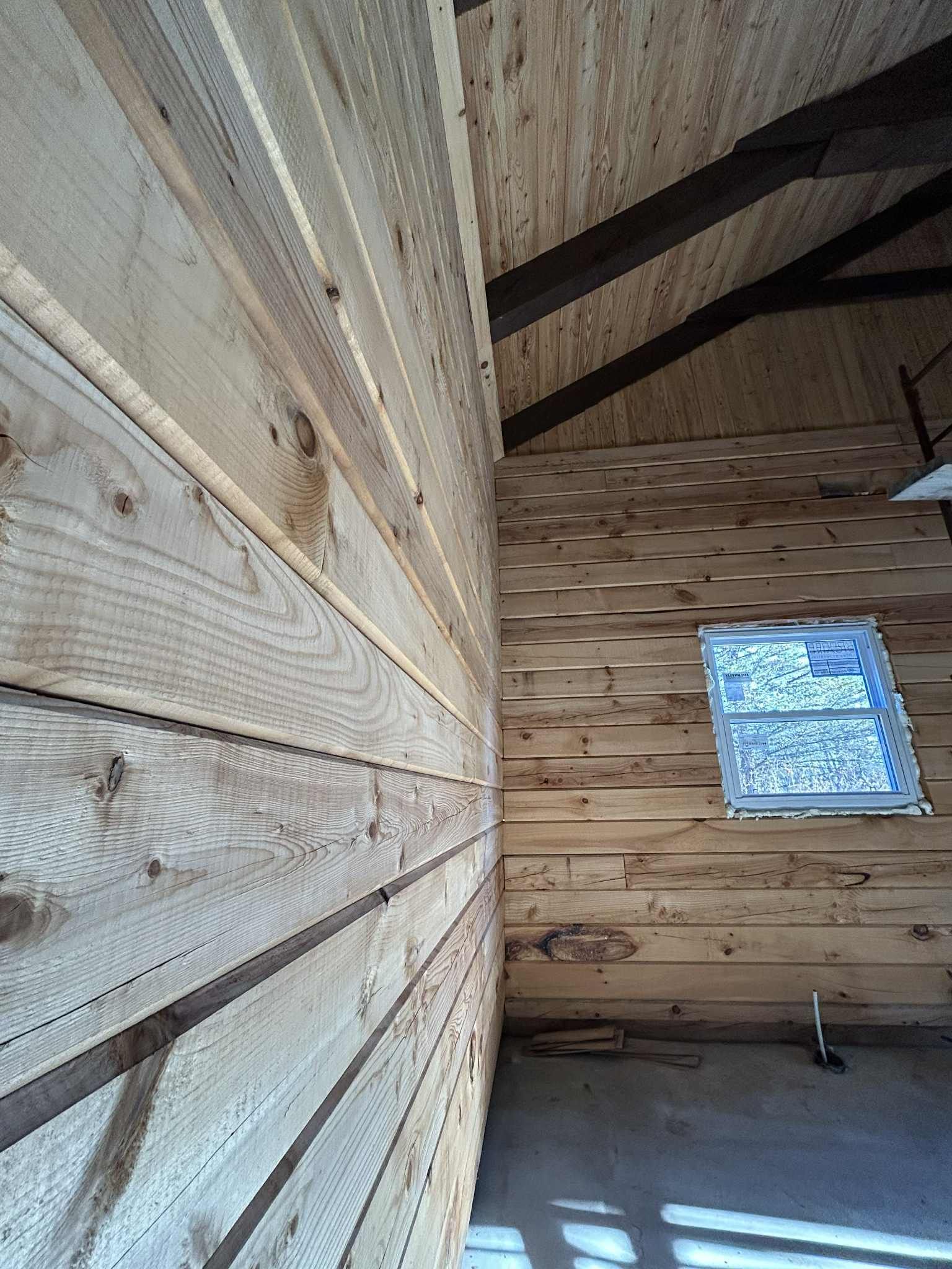 Intérieur en bois avec murs et plafond à lattes, une fenêtre et des poutres sombres.