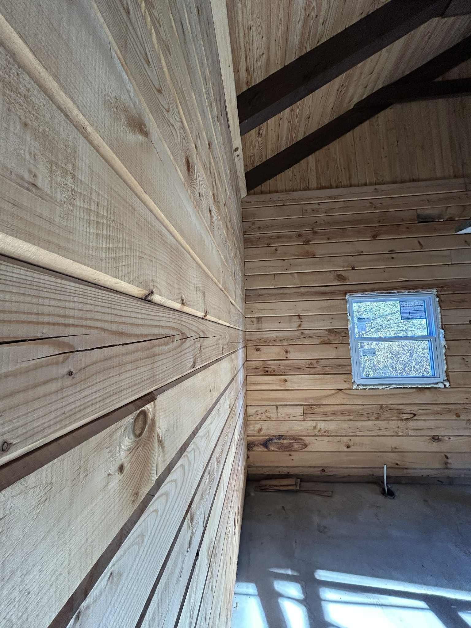 Intérieur en bois en cours d'aménagement. Planches de bois brut aux murs et au plafond, petite fenêtre visible.