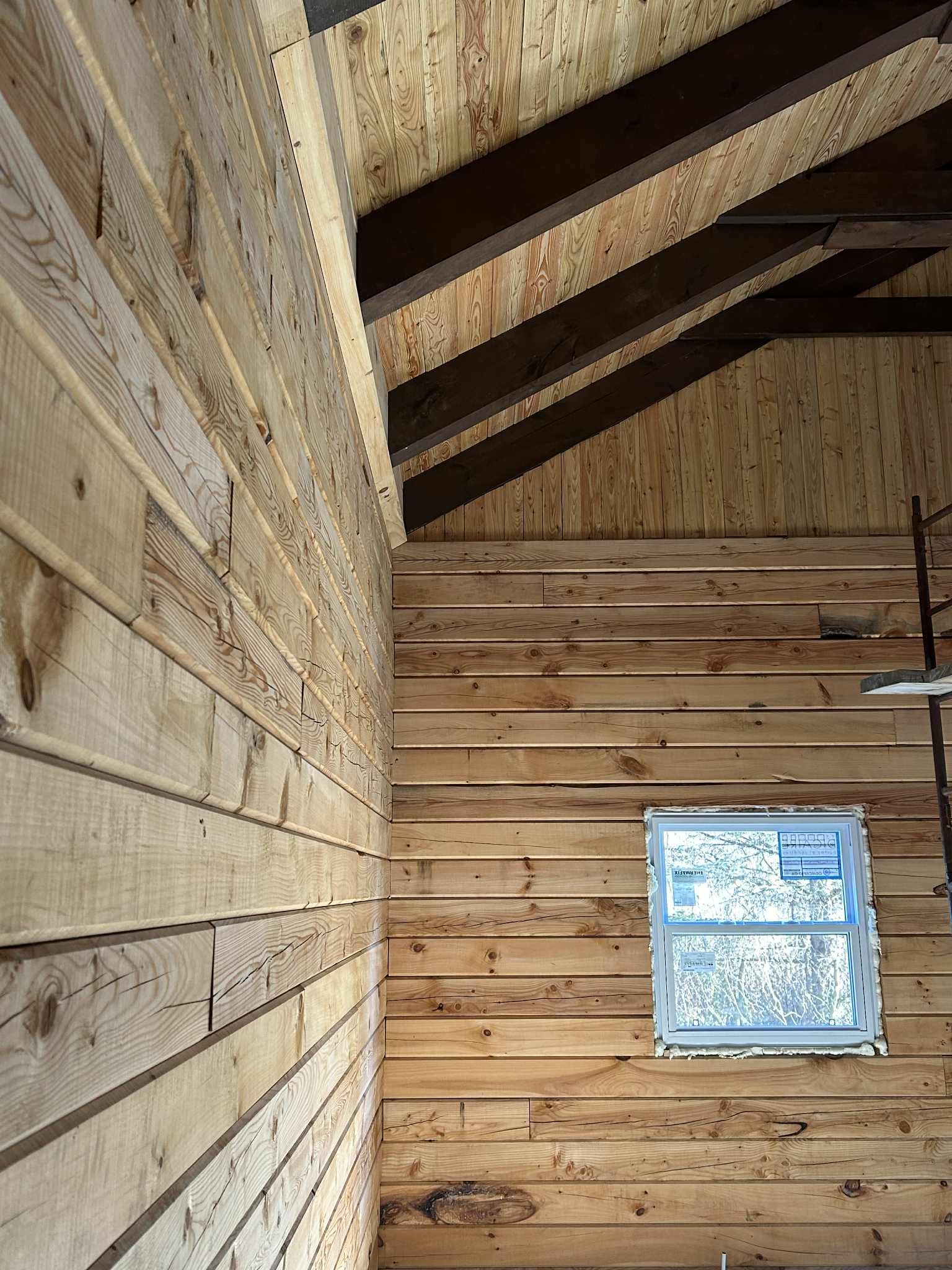 Intérieur d'une pièce lambrissée avec fenêtre. Poutres et chevrons apparents au plafond.