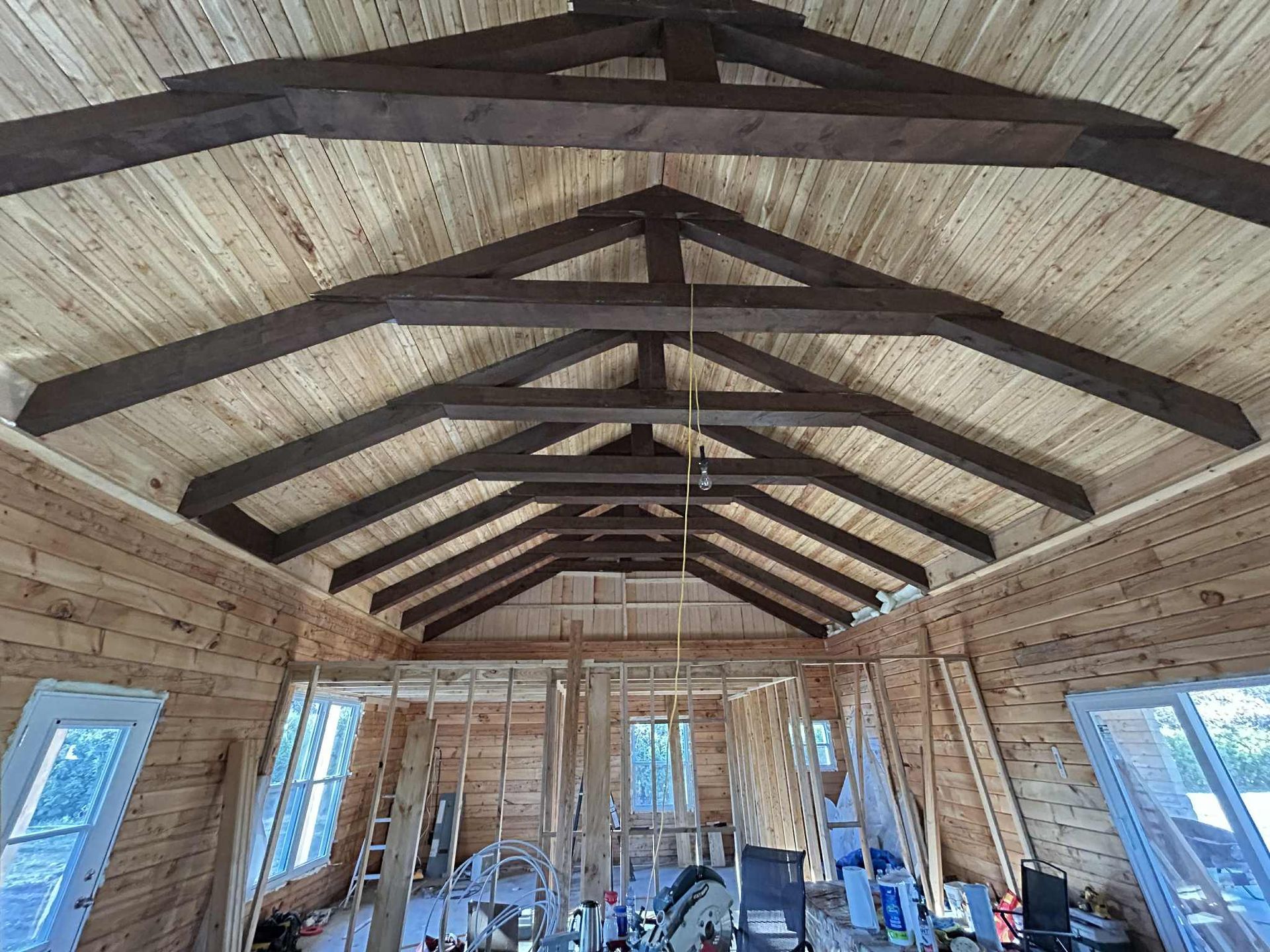 Vue intérieure d'une construction en bois, mettant en valeur les poutres du plafond et les murs. Le bois clair domine, avec des poutres brun foncé.