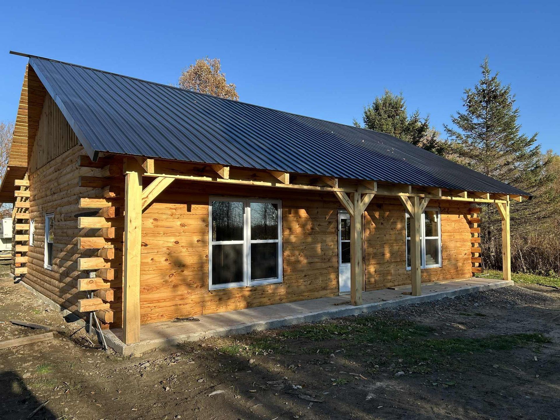 Cabane en rondins en construction, avec toit en métal foncé et porche couvert.