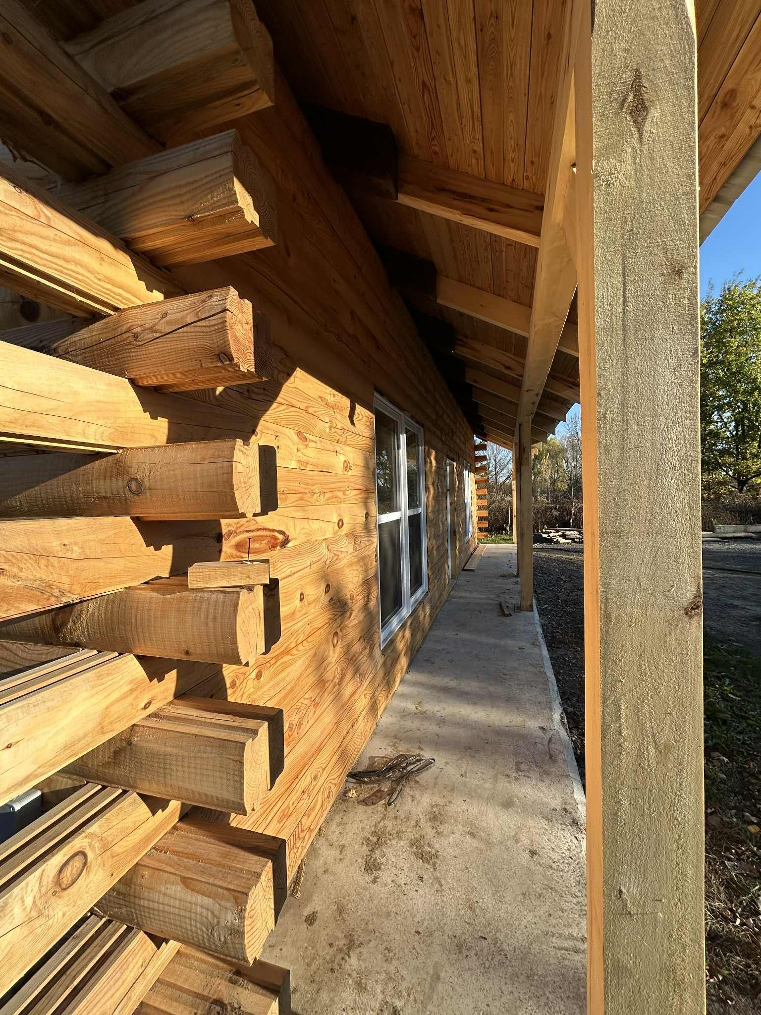 Chalet en rondins en construction avec porche, bois et béton.