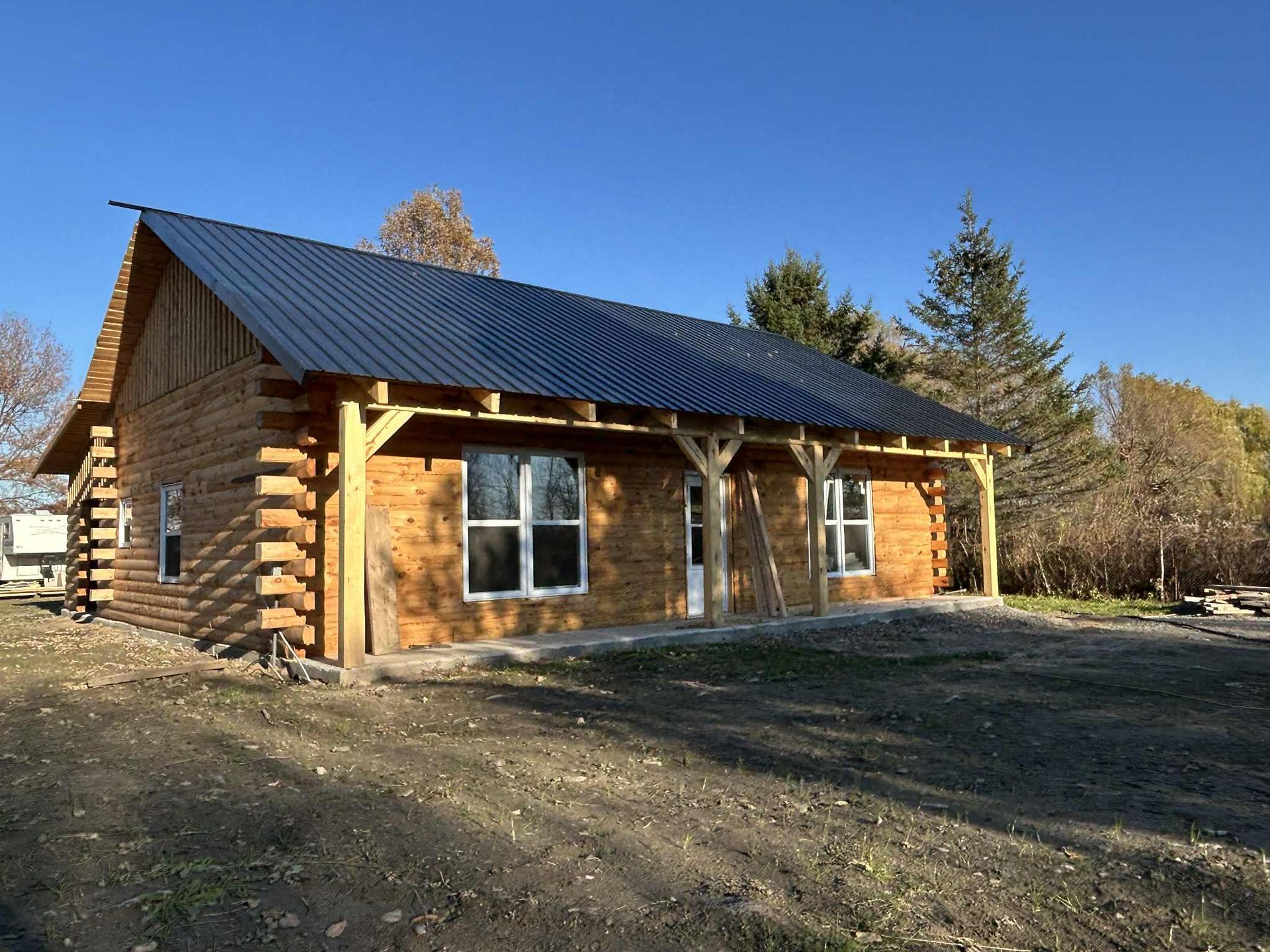 Chalet en rondins avec toit et porche noirs, par une journée ensoleillée.