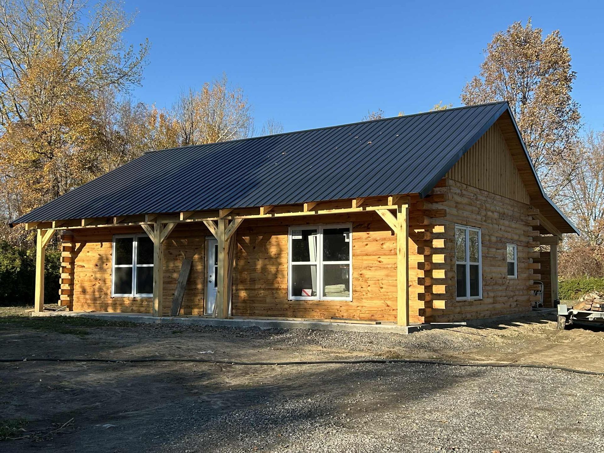 Construction d'une maison en bois avec un toit en tôle bleue sur un terrain gravillonné sous un ciel bleu.
