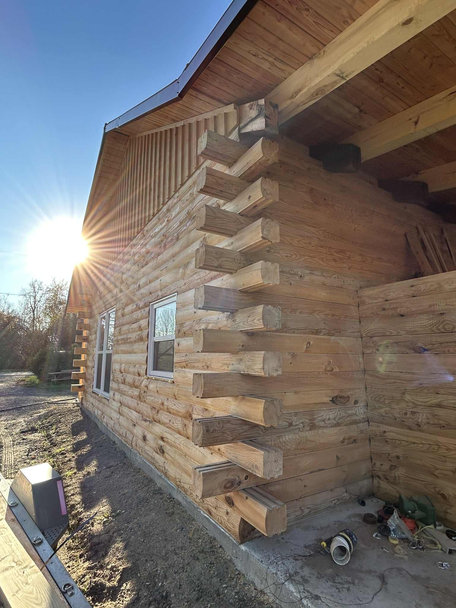 Cabane en rondins en construction, baignée d'un soleil éclatant, laissant apparaître les angles en rondins et les fenêtres.