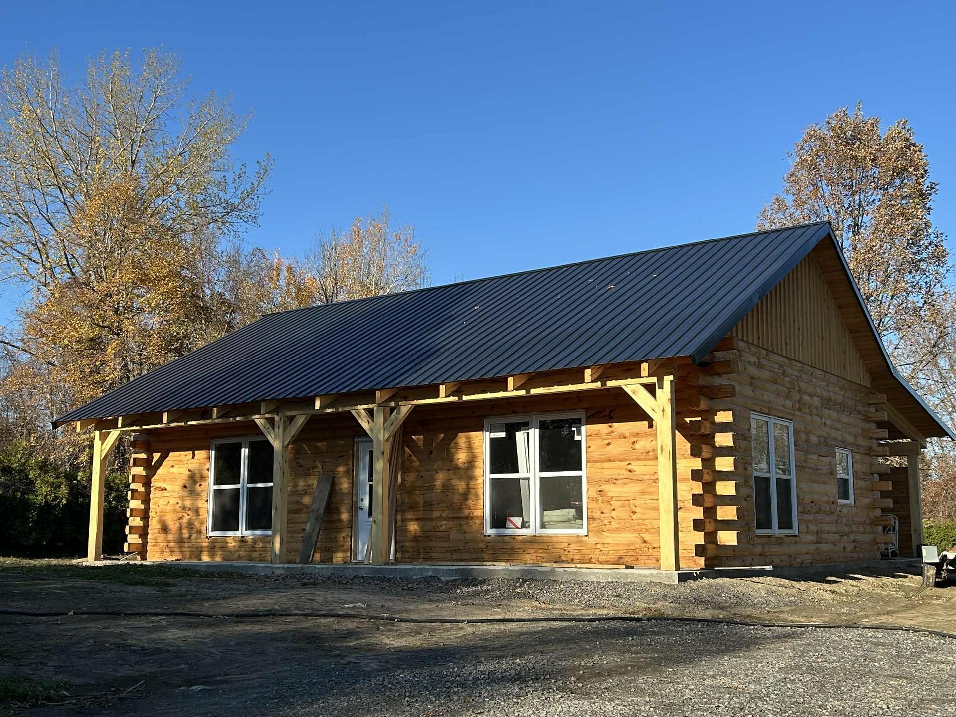 Cabane en rondins en construction avec toit en métal bleu foncé, porche et fenêtres.