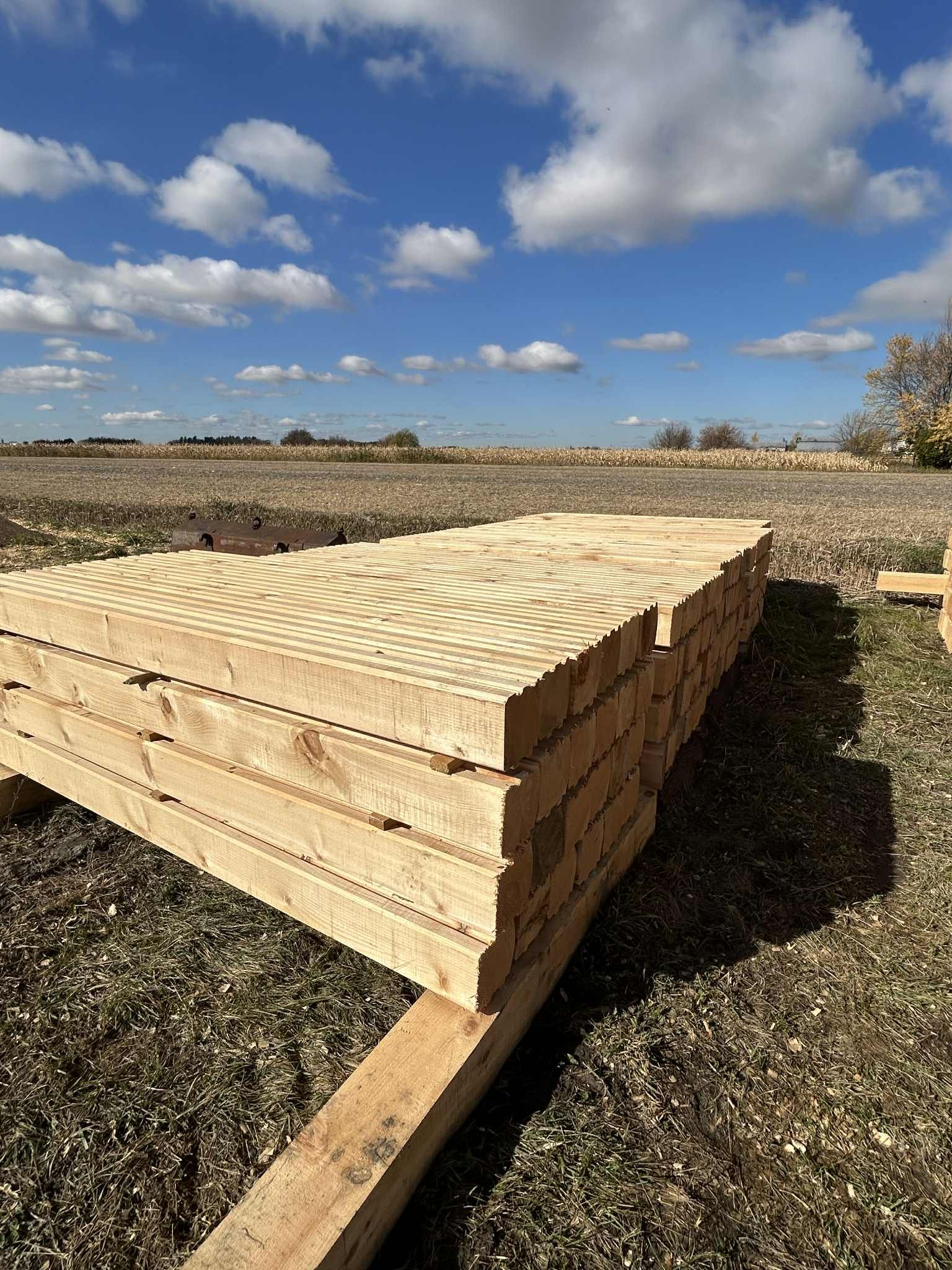 Pile de planches de bois à l'extérieur, sous un ciel bleu, sur un support en bois.