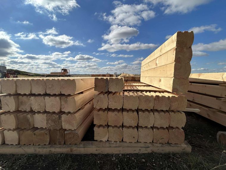 Des piles de blocs de bois clair à l'extérieur, sous un ciel bleu partiellement nuageux.