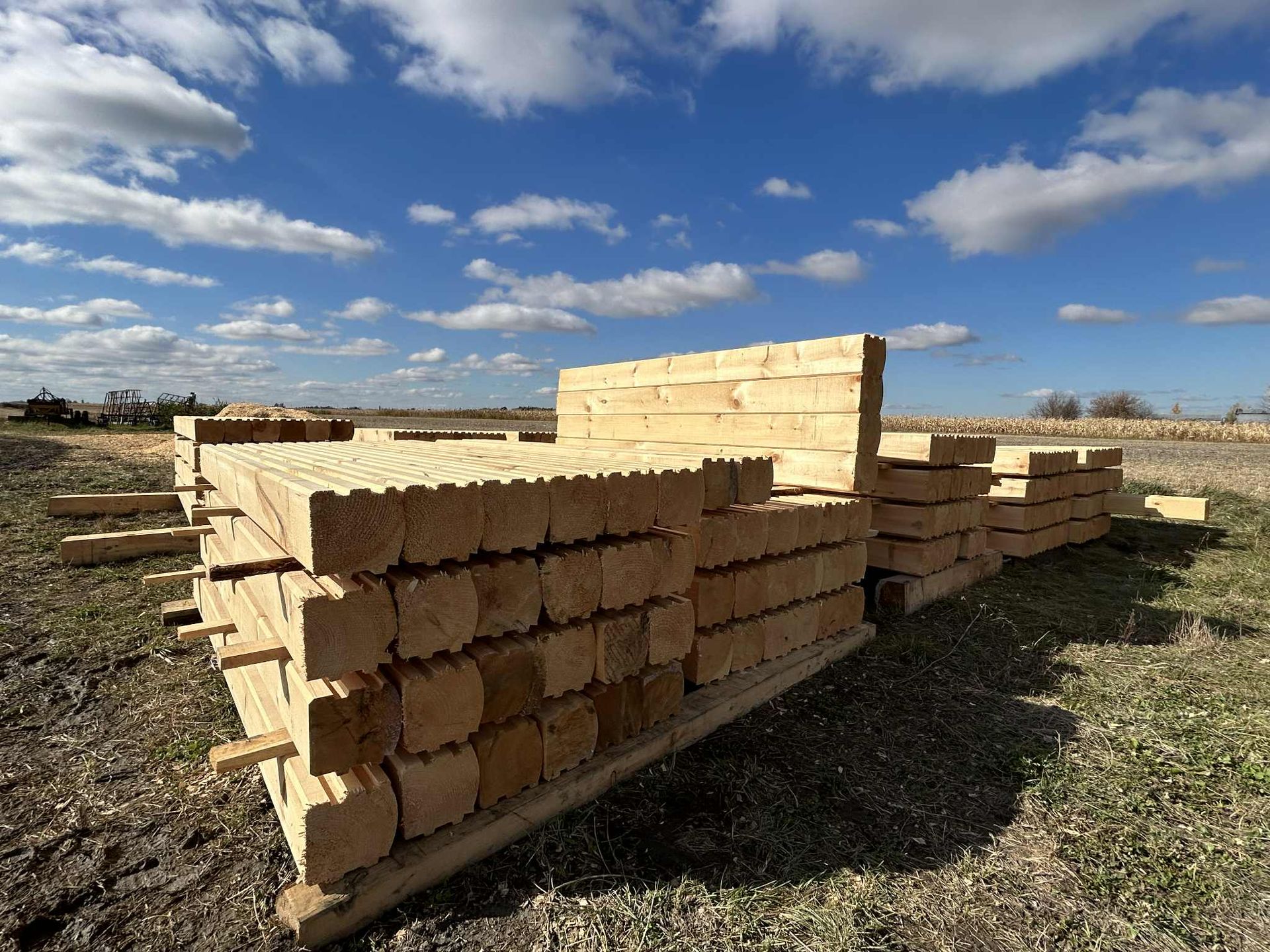 Des bûches de bois empilées à l'extérieur, sous un ciel bleu, prêtes pour la construction.