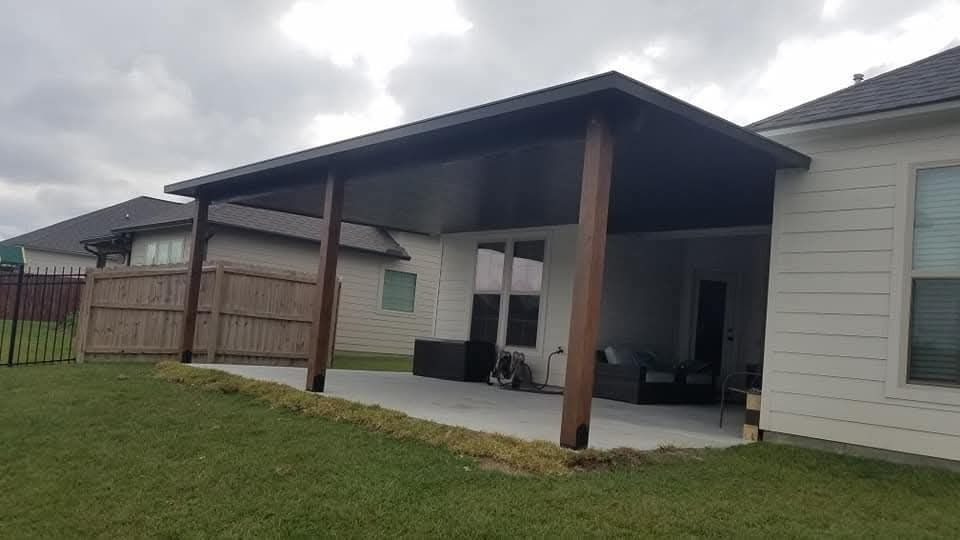 Covered patio attached to a single-story house with brown posts and outdoor seating on a grassy lawn