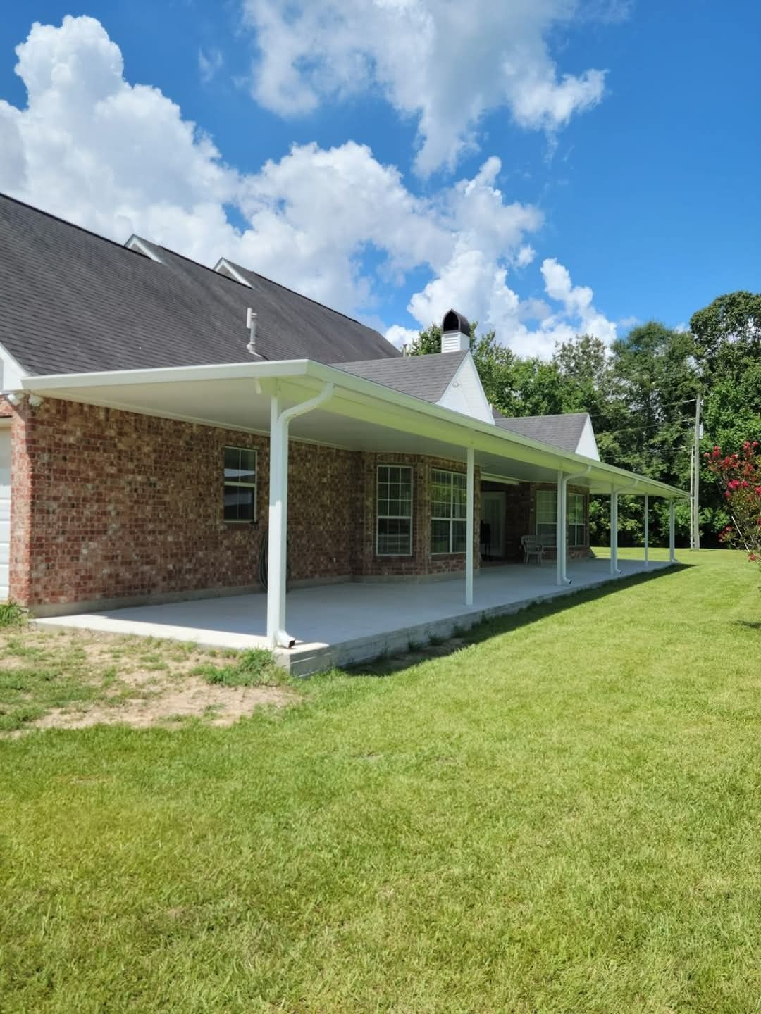Brick house with a white porch and green lawn under a blue sky with clouds