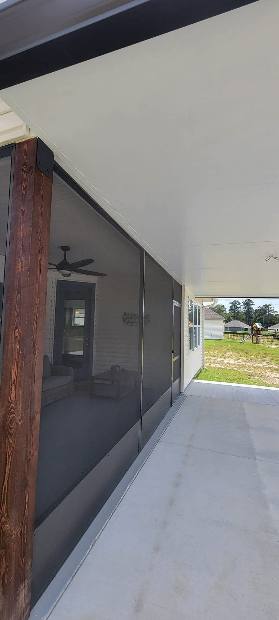 Covered walkway beside a modern building with dark windows and a tiled sidewalk leading to grass ahead