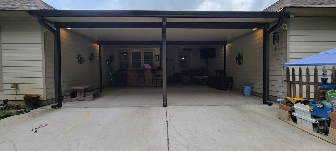 Open garage with two parked cars, concrete driveway, and storage items along the sides