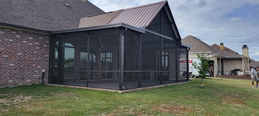 Screened porch attached to a brick house with a sloped roof and grassy yard outside.