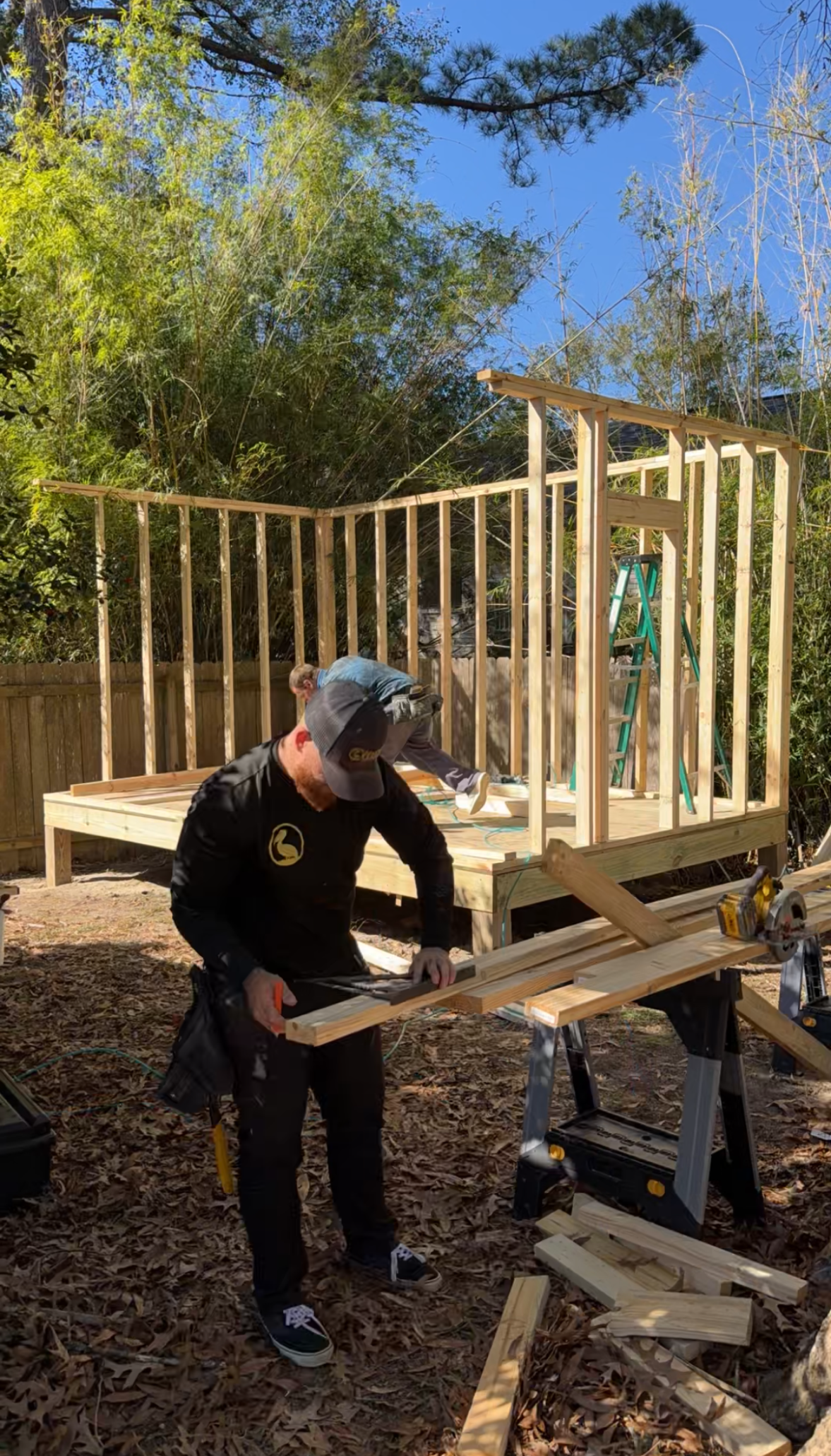 Person working on a wooden deck frame in a sunny outdoor yard