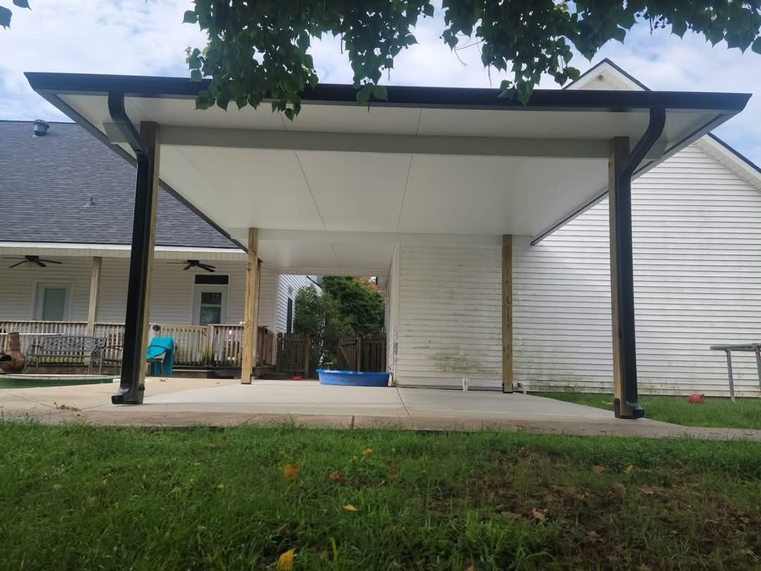 Covered patio/carport beside a house, with a blue planter, white siding, and grass in front.