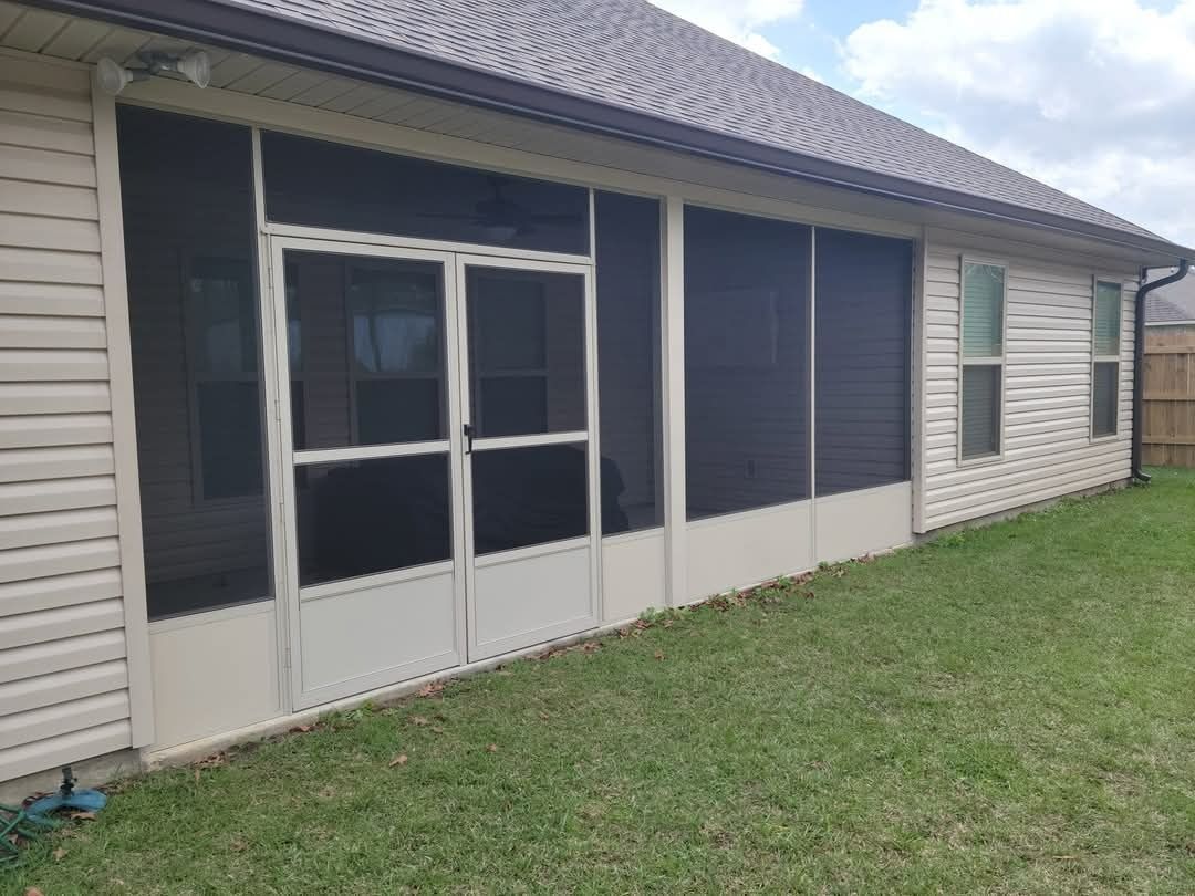 Single-story beige house with screened windows and a screened patio, viewed from the backyard lawn.