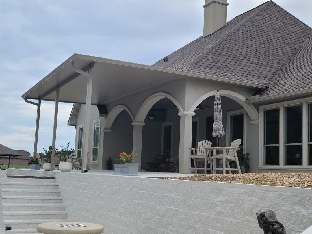 White stucco house with arched porch, stairs, and outdoor seating on a raised patio.