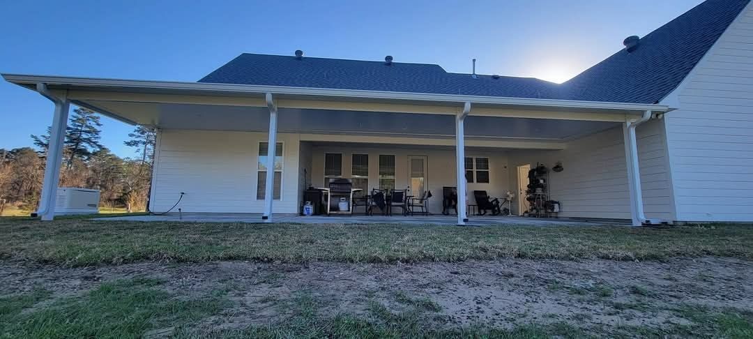 Wide white farmhouse with blue roof and porch, set on a grassy yard at dusk.