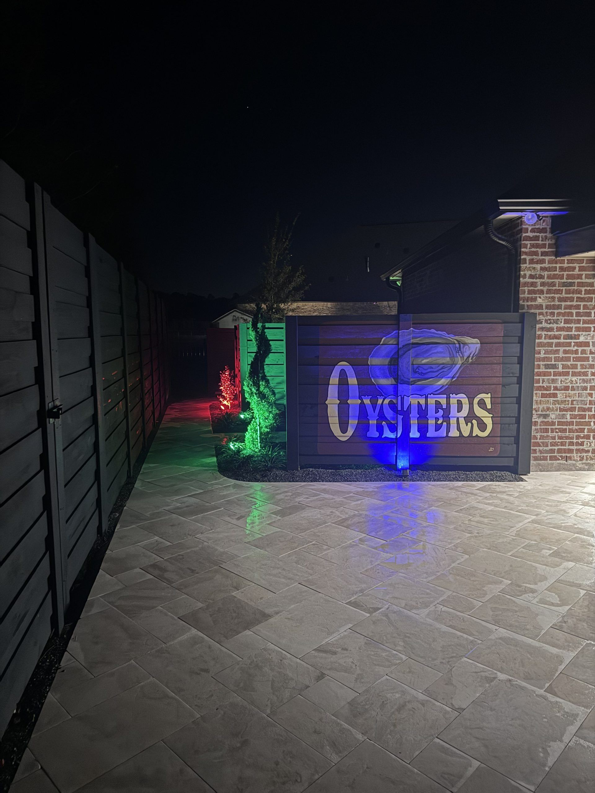 Nighttime patio sign for Oysters with blue and green light projections on brick walls