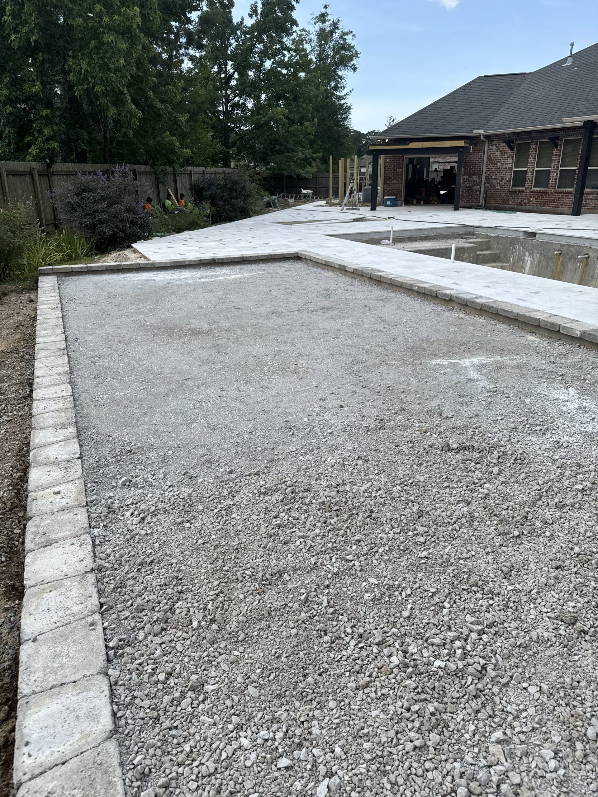 Gravel driveway beside a brick house and trees, bordered by concrete curbs.