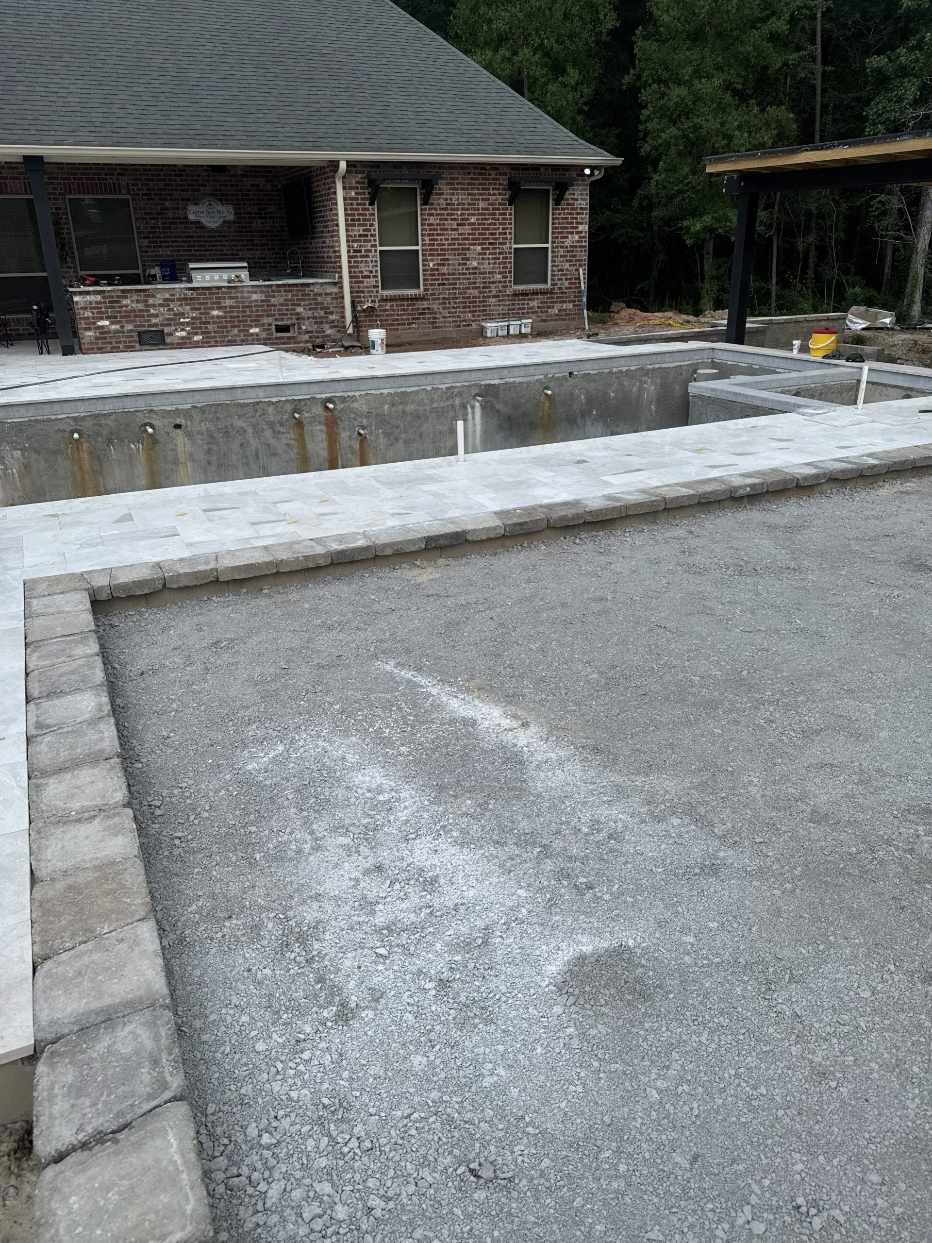 Stone retaining wall and gravel driveway beside a brick building and trees outdoors